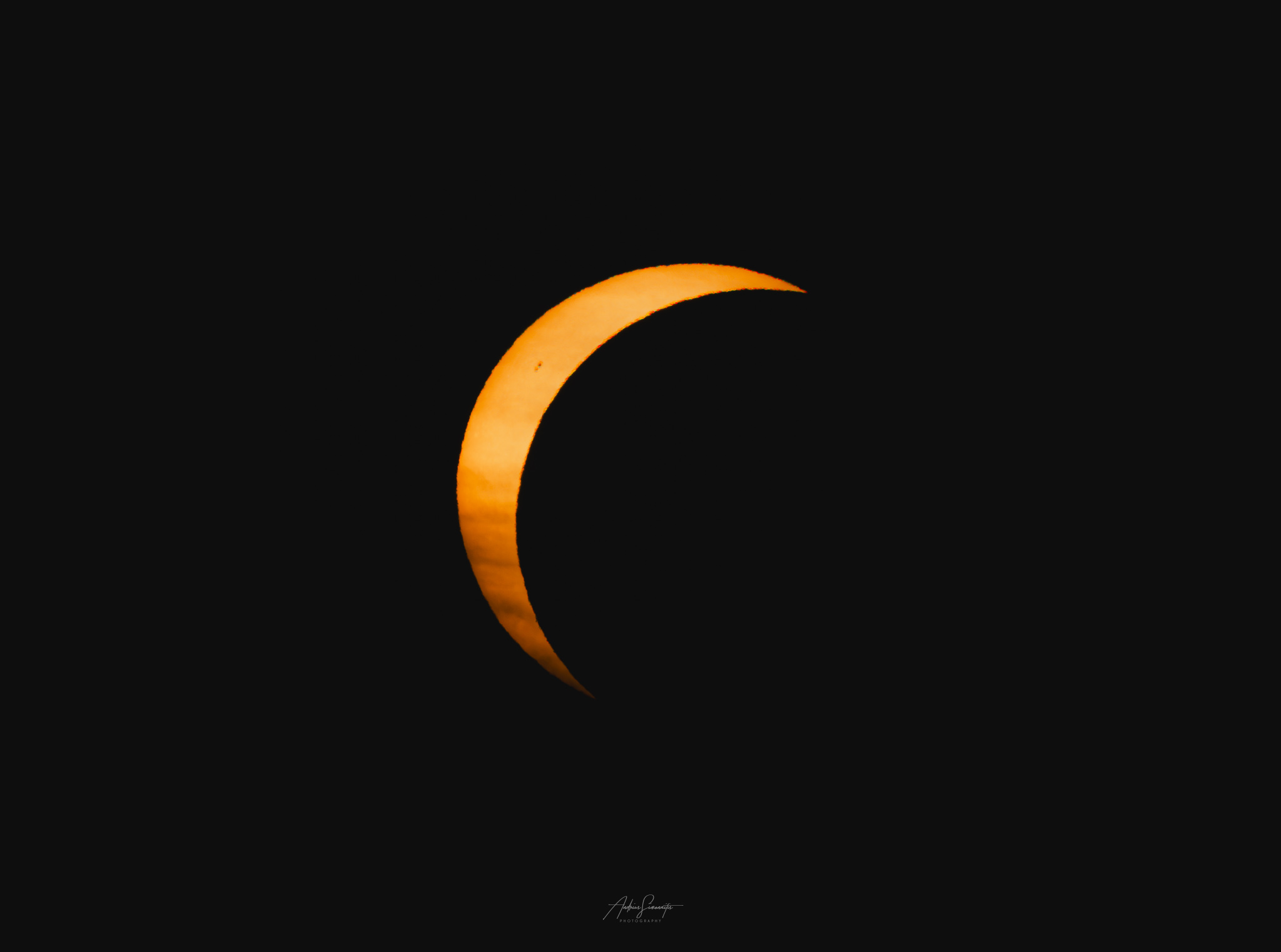 A bright orange crescent of the sun against a black sky