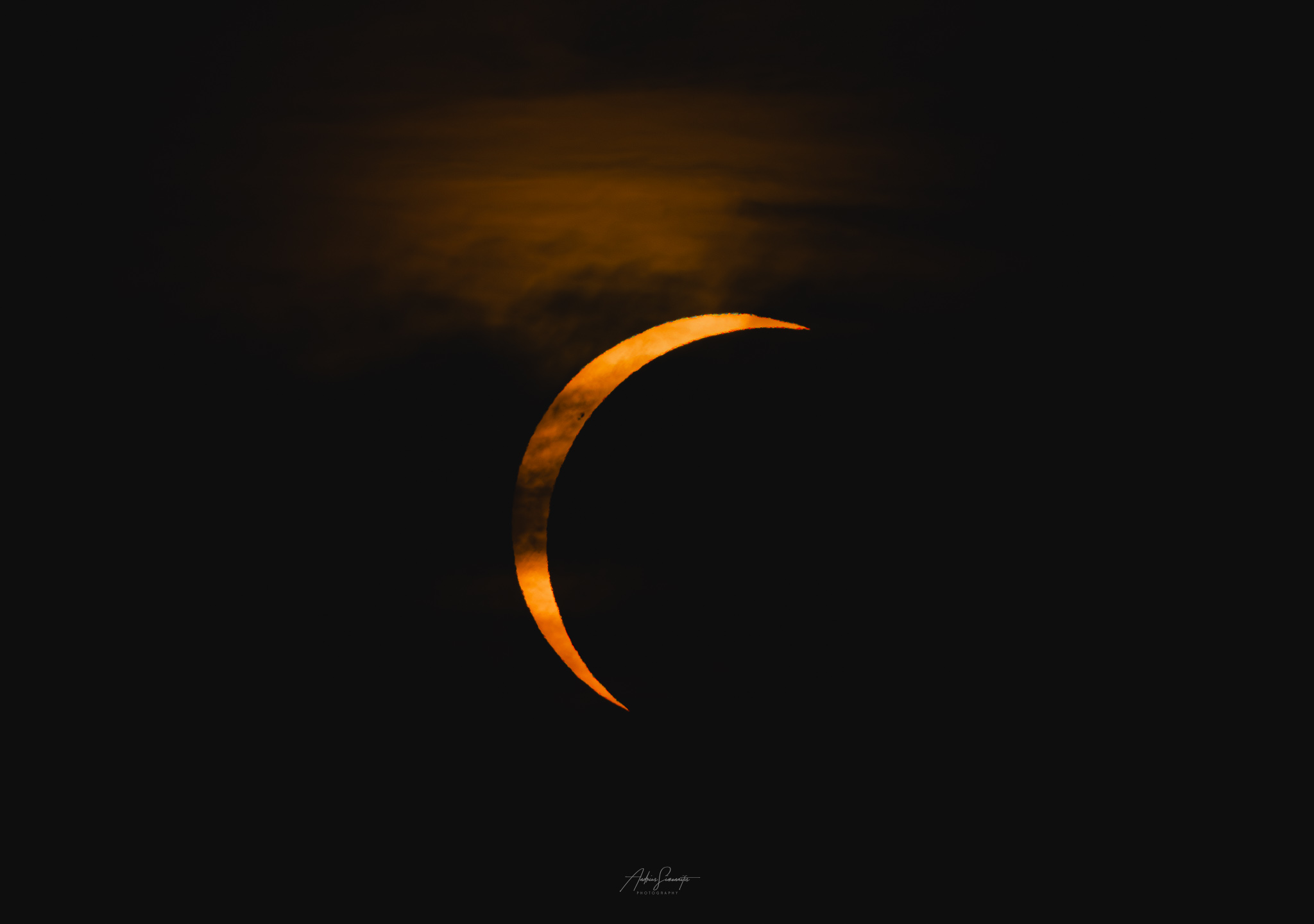 Orange solar crescent cutting through dark clouds