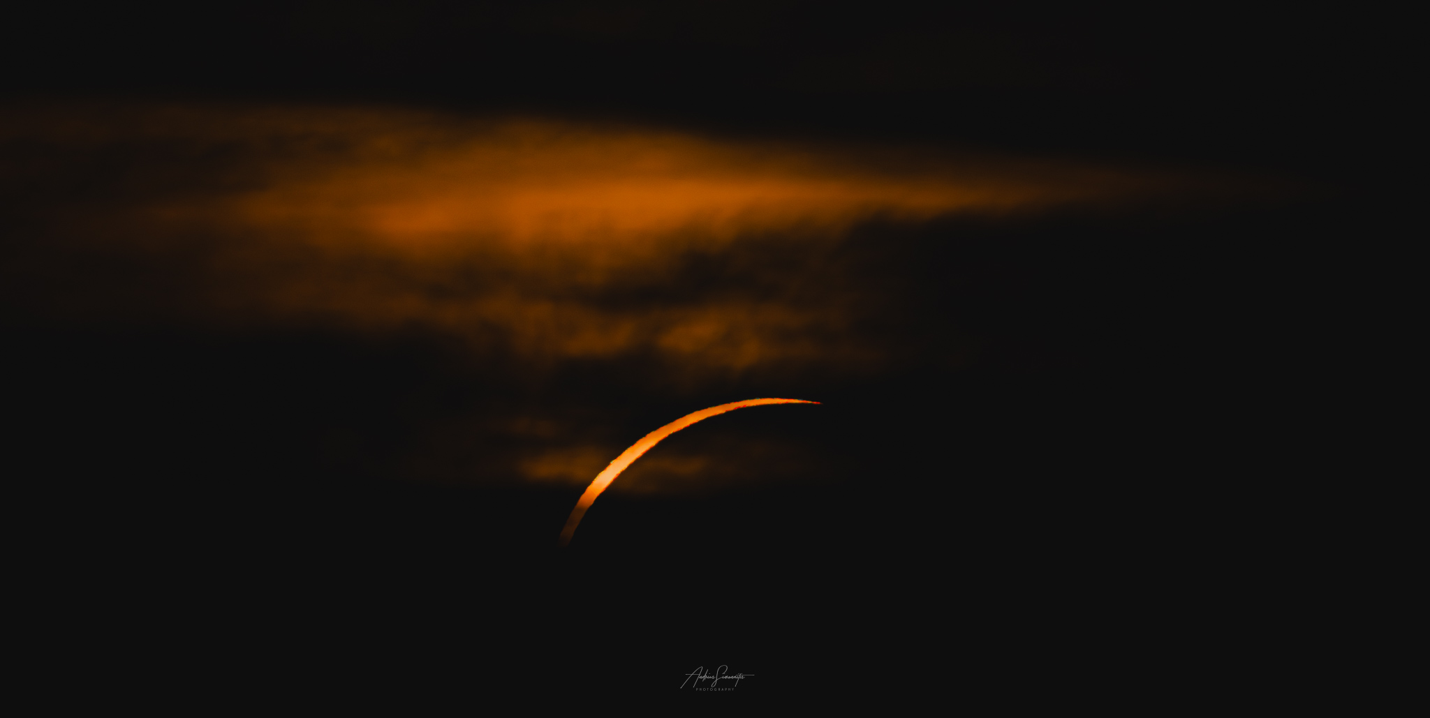 A thin orange solar crescent behind glowing dark clouds